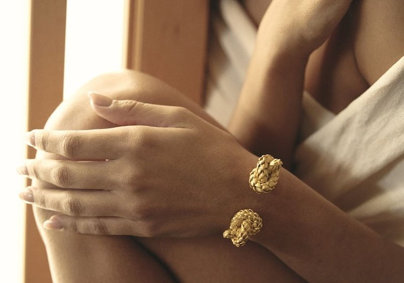 Close up image of a woman wearing two rings - one gold and one silver.  She's also wearing a matching bracelet in gold. The purpose of this image is to highlight the rings and bracelet by ALMA Jewelry.