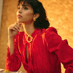 Image of a woman wearing a red dress, gold earrings and a matching pin. The purpose of this image is to highlight the earrings by Alma jewelry.