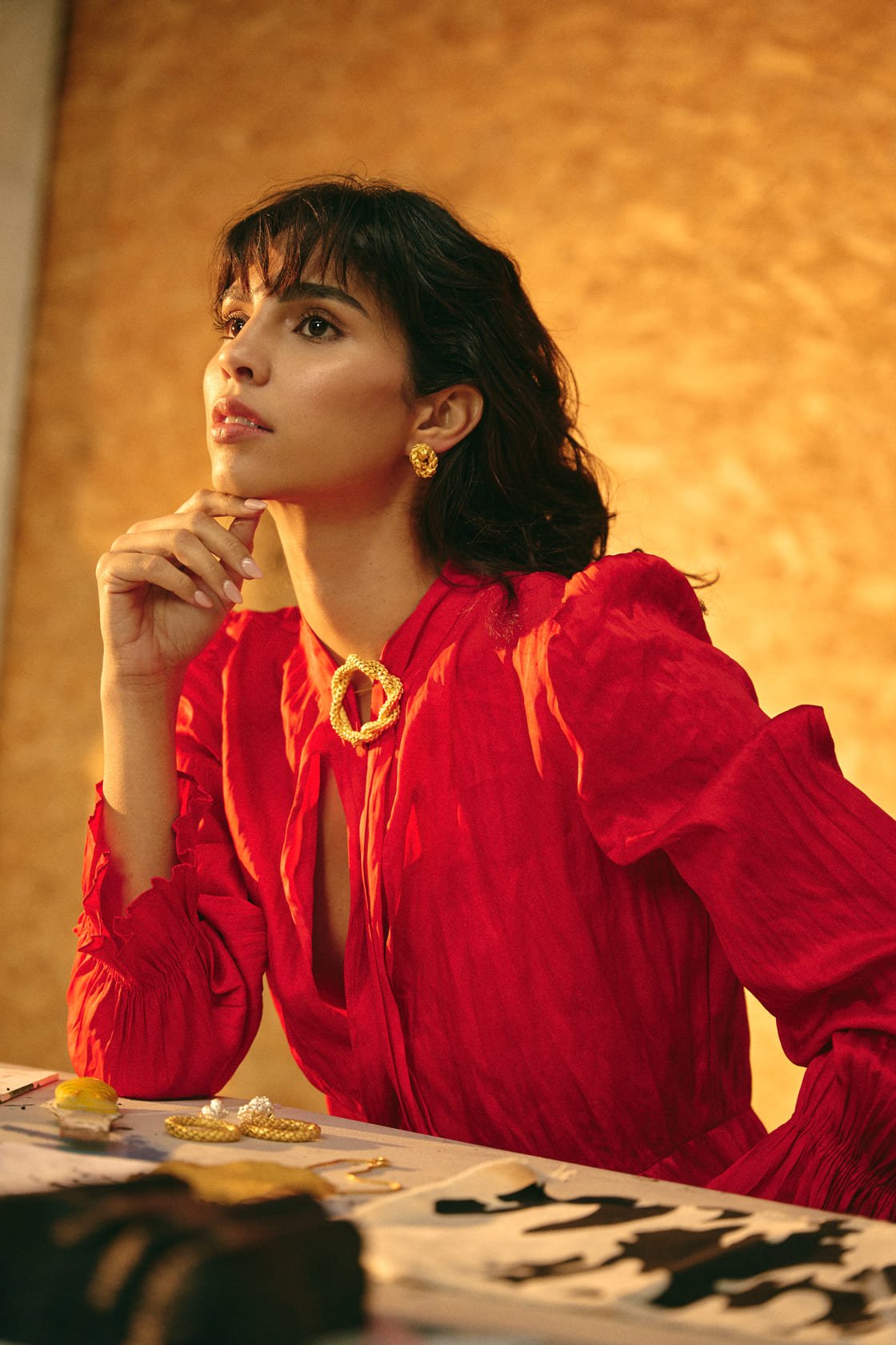 Image of a woman wearing a red dress, gold earrings and a matching pin. The purpose of this image is to highlight the earrings by Alma jewelry.