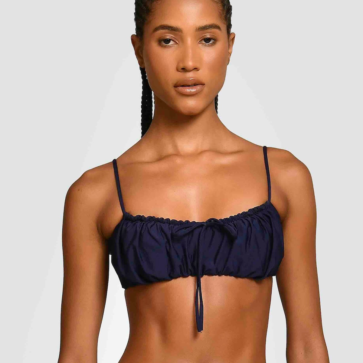 Woman wearing a navy blue bandeau bikini top against a plain background