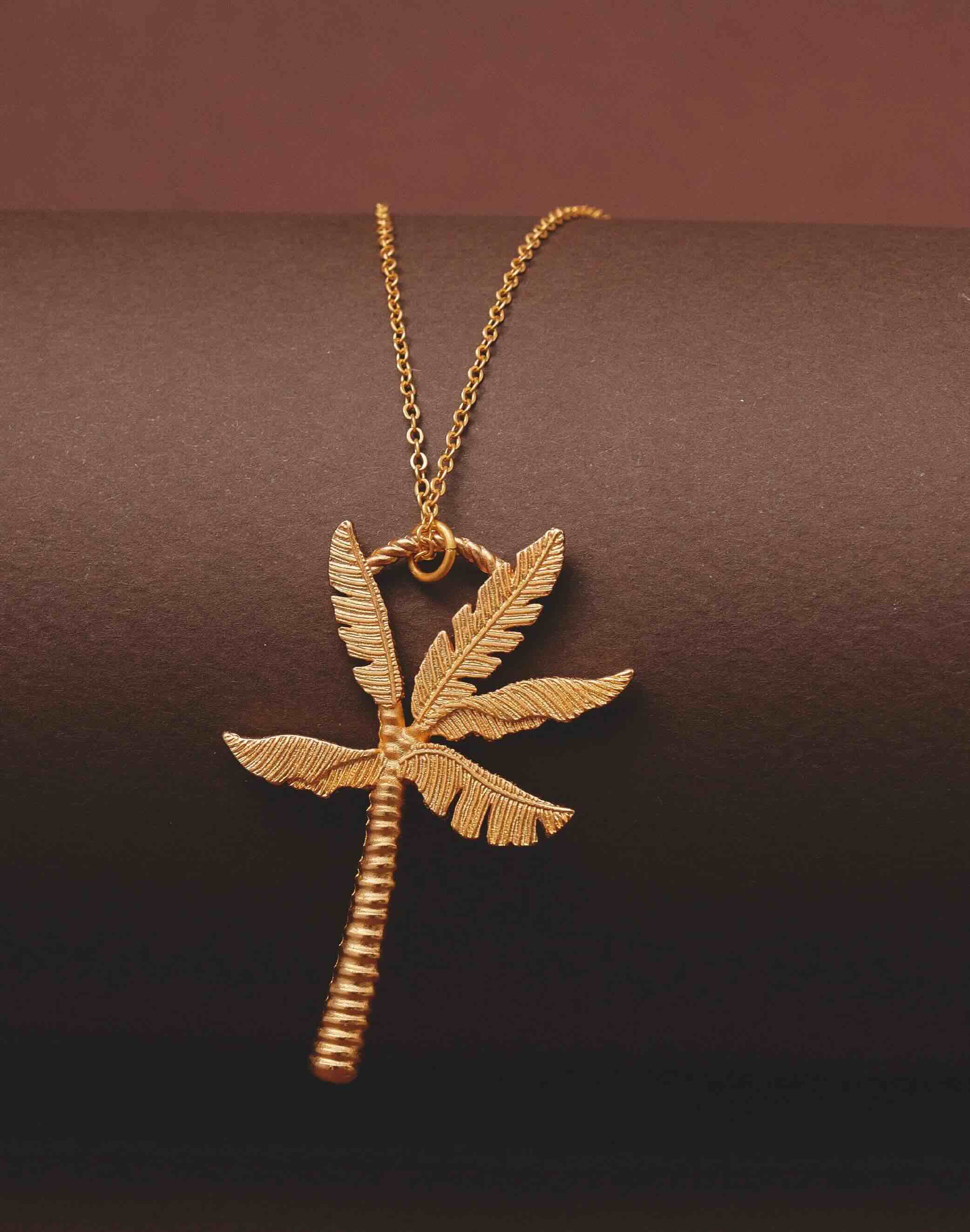 Gold palm tree necklace on a dark brown background