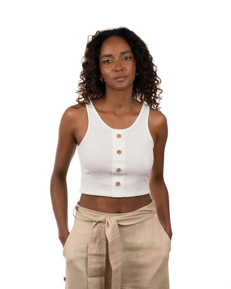 Woman wearing a white ribbed top and black bottoms. She's standing by a white background and looking at the camera. The purpose of this image is to highlight the sustainable clothing by Madre Tierra.