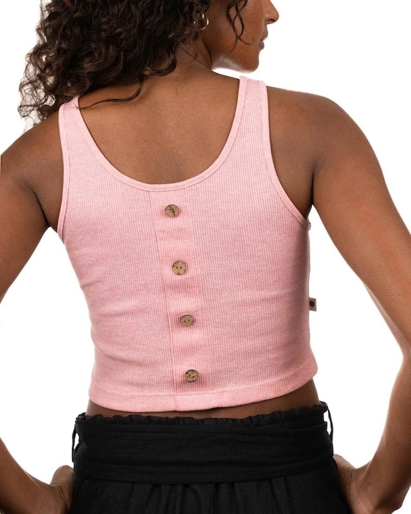 Back of a woman wearing a pink ribbed top and black bottoms. She's standing by a white background and looking at the camera. The purpose of this image is to highlight the sustainable clothing by Madre Tierra.