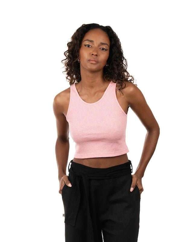 Woman wearing a pink ribbed top and black bottoms. She's standing by a white background and looking at the camera. The purpose of this image is to highlight the sustainable clothing by Madre Tierra.