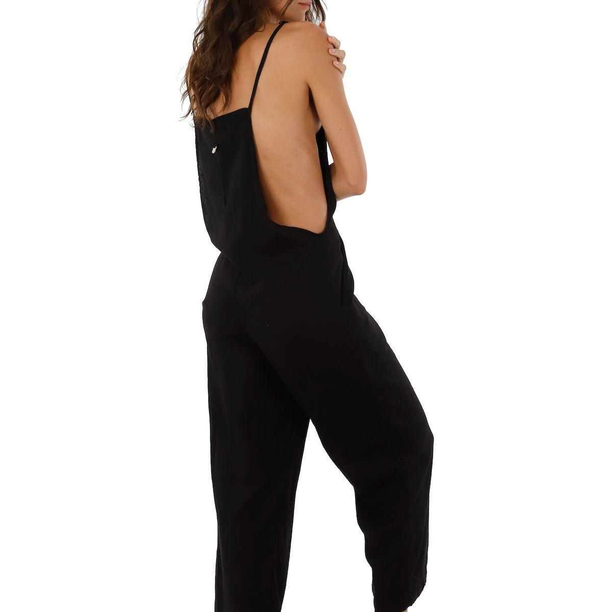 Image of a woman wearing a black jumpsuit. She's looking to the side and standing against a white background. The purpose of this image is to highlight the jumpsuit.