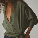 Woman wearing a green wrap top with a plain background