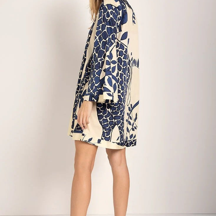 Model wearing a giraffe print cover-up dress with long sleeves. She's standing against a white background and looking at the camera. The purpose of this image is to highlight the dress.