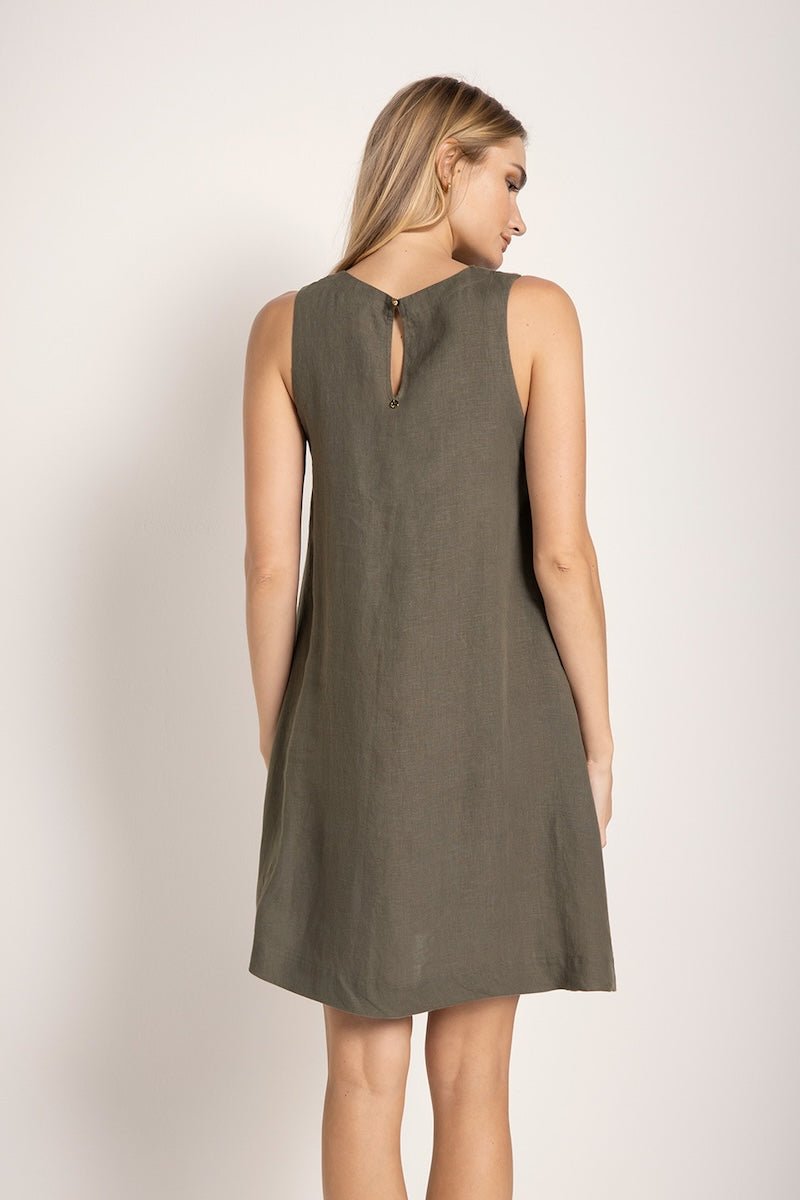 Image of a woman wearing a short linen dress that is brown/grey in color. She's standing against a white background and looking to the side. We're able to see her back. The purpose of this image is to highlight the dress.