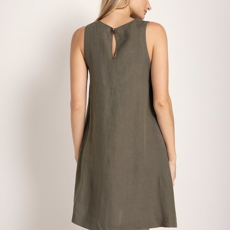 Image of a woman wearing a short linen dress that is brown/grey in color. She's standing against a white background and looking to the side. We're able to see her back. The purpose of this image is to highlight the dress.