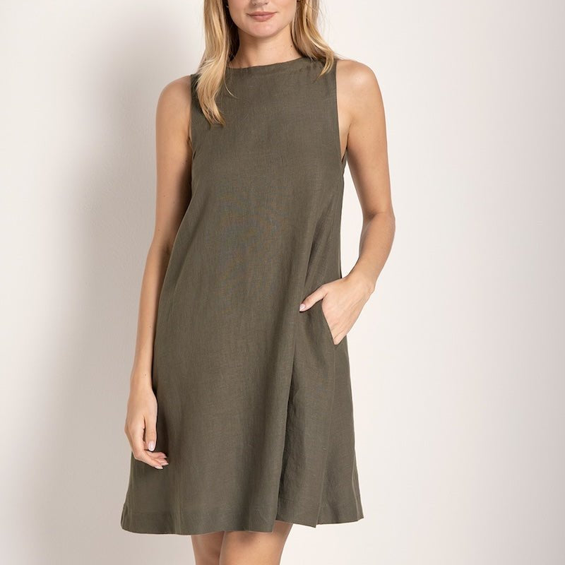 Image of a woman wearing a short linen dress that is brown/grey in color. She's standing against a white background and has one hand on her pocket. The purpose of this image is to highlight the dress.