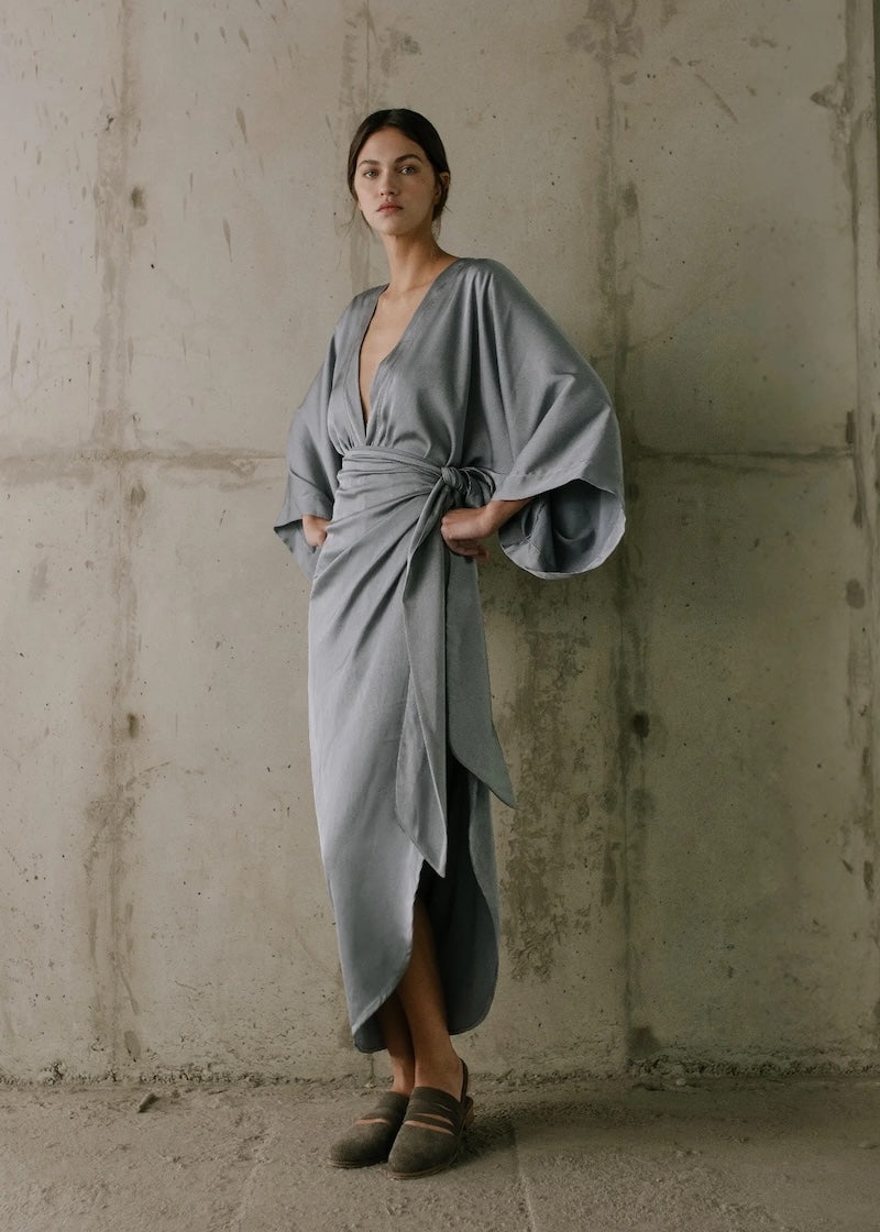 Woman wearing a gray dress against a textured wall.