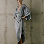 Woman wearing a gray dress against a textured wall.
