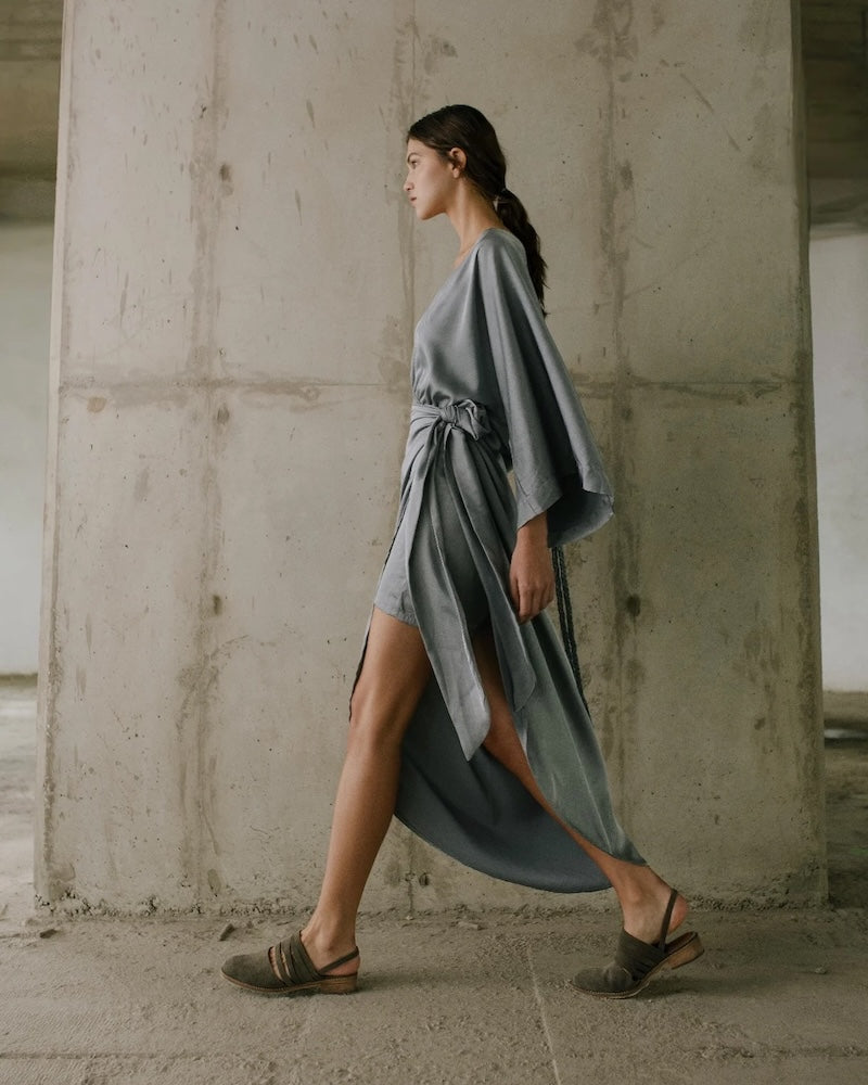 Woman in a long, light gray dress walking in an industrial setting.
