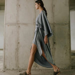 Woman in a long, light gray dress walking in an industrial setting.