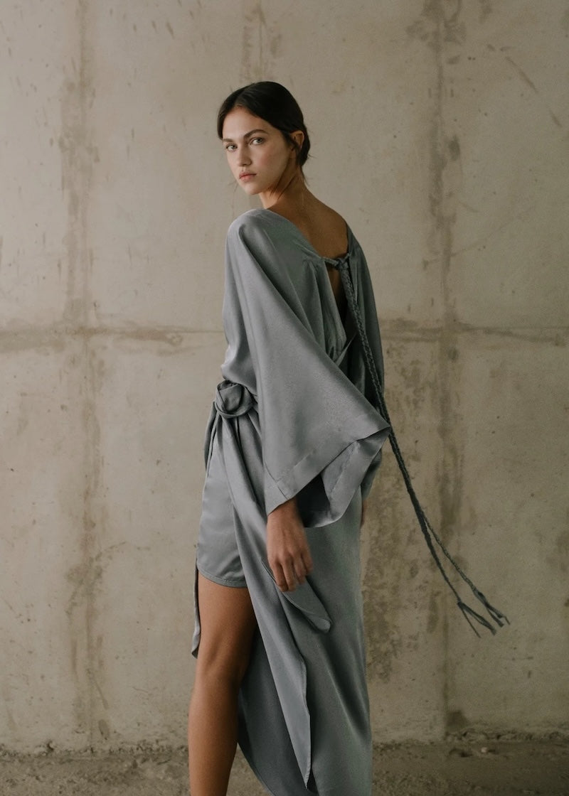 Woman wearing a gray dress against a textured wall.