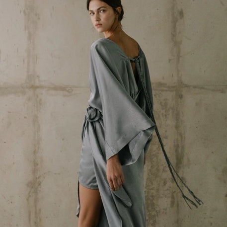 Woman wearing a gray dress against a textured wall.