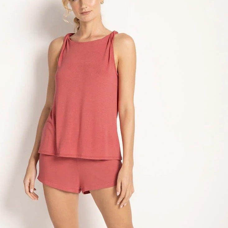 Model wearing a rose colored pajama set. The top is sleeveless and the shorts are stretchy. She's standing in front of a white wall. The purpose of this image is to highlight the clothing.