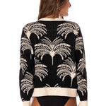 Woman wearing a black and white sweater with palm tree pattern on a white background.