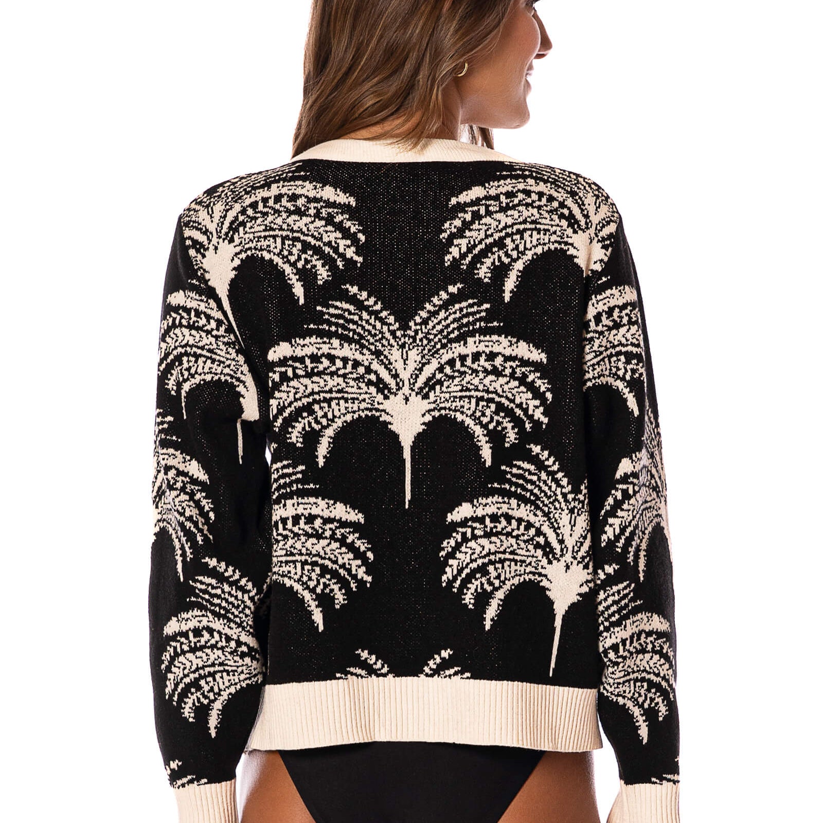 Woman wearing a black and white sweater with palm tree pattern on a white background.