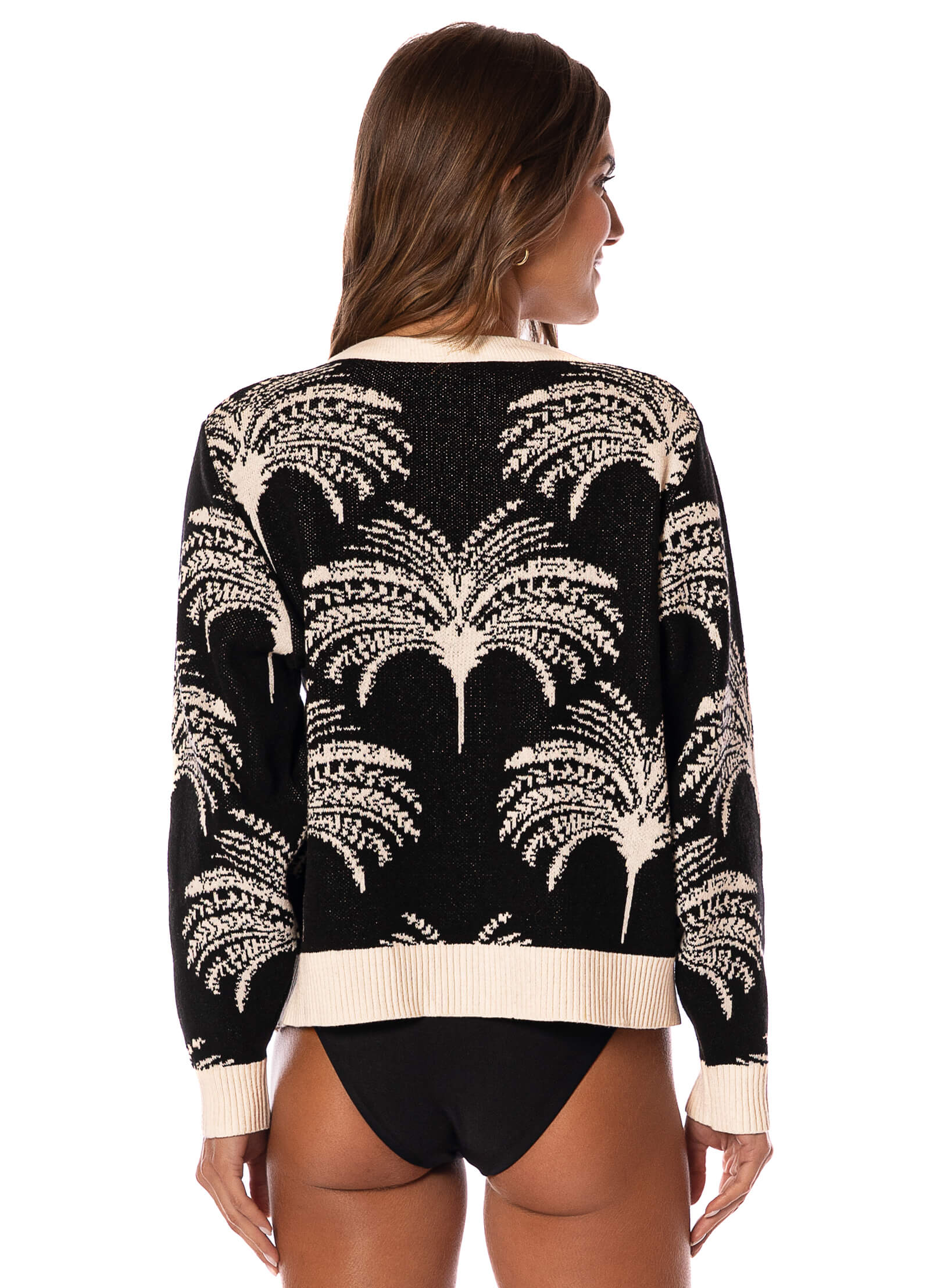 Woman wearing a black and white sweater with palm tree pattern on a white background.