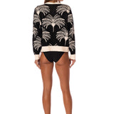 Woman wearing a black tree palm patterned sweater and black underwear on a white background.