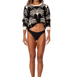 Woman wearing a black and white tree palm patterned sweater and black bikini bottom on a white background.