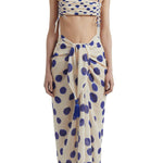 Woman wearing a bikini top with blue polka dots and a matching sarong. She's standing behind a white background. The purpose of this image is to highlight the sarong by Encantadore Swimwear.