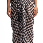 Close up image of a woman wearing a black and white sarong. She's standing behind a white background. The purpose of this image is to highlight the sarong by Encantadore Swimwear.