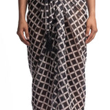 Close up image of a woman wearing a black and white sarong. She's standing behind a white background. The purpose of this image is to highlight the sarong by Encantadore Swimwear.