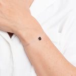 Image of a woman wearing a thin thread with a black tourmaline stone in the center as a bracelet. The purpose of this image is to highlight the product (a threaded necklace and bracelet) because it is for sale at EVAMAIA boutique in Studio City, CA and online.