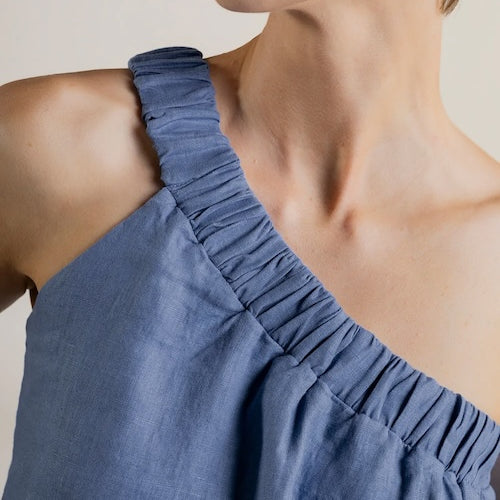 Close-up of a person wearing a blue one-sleeve top against a white background.