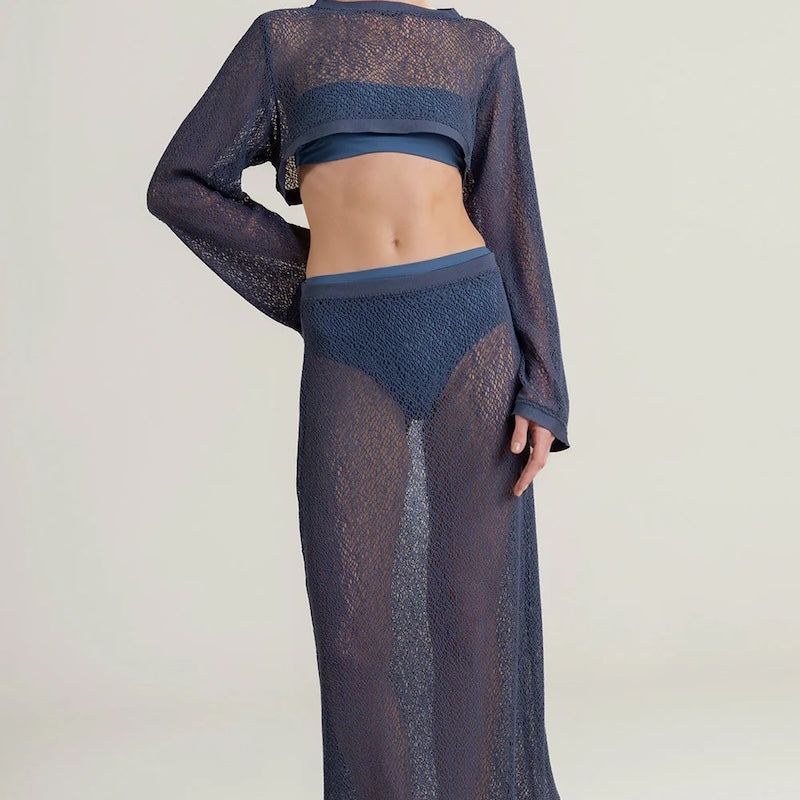 Woman wearing a dark blue sheer top with a matching maxi skirt on a light background. 