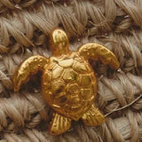 Gold turtle pendant on a textured beige background