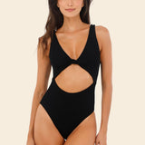 Woman wearing a black cut-out swimsuit on a beige background