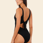 Back of a woman wearing a black swimsuit with cut-out design on a beige background