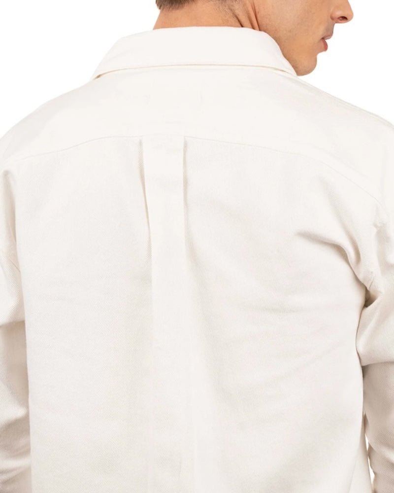 Close up of the back of a man wearing a white cotton jacket. He's standing behind a white background. The purpose of this image is to highlight the jacket, which is made in Colombia and available at EVAMAIA boutique.