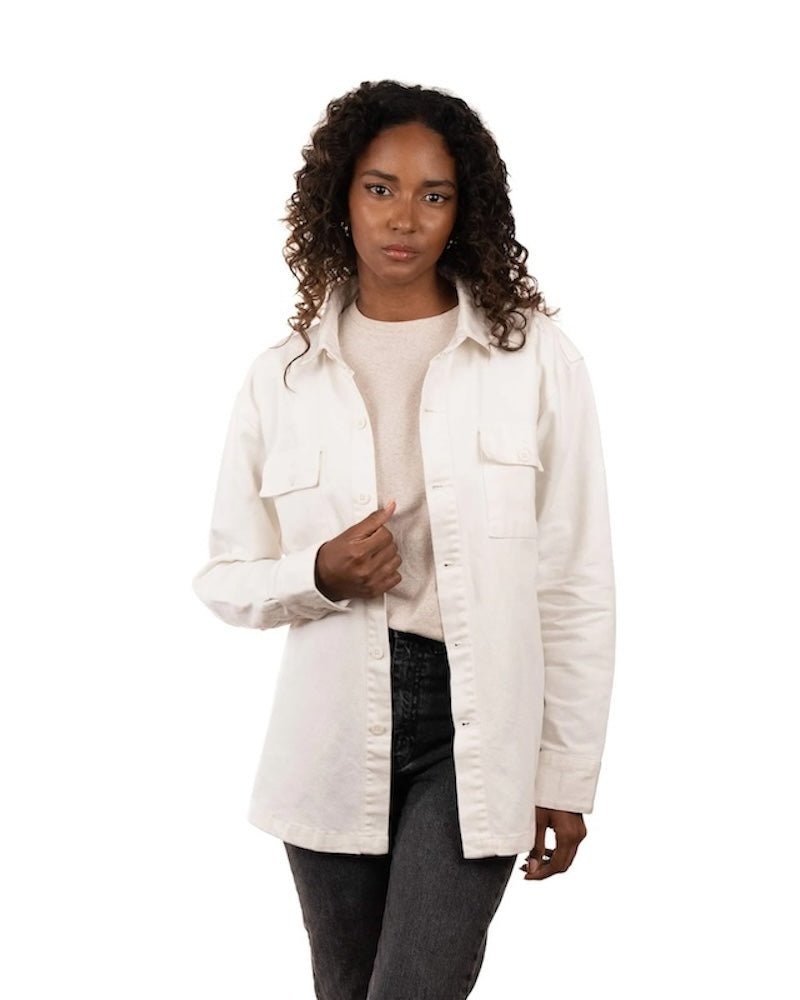 Woman wearing jeans, a t-shirt and a white jacket. She's standing behind a white background. The purpose of this image is to highlight the jacket, which is made in Colombia and available at EVAMAIA boutique.