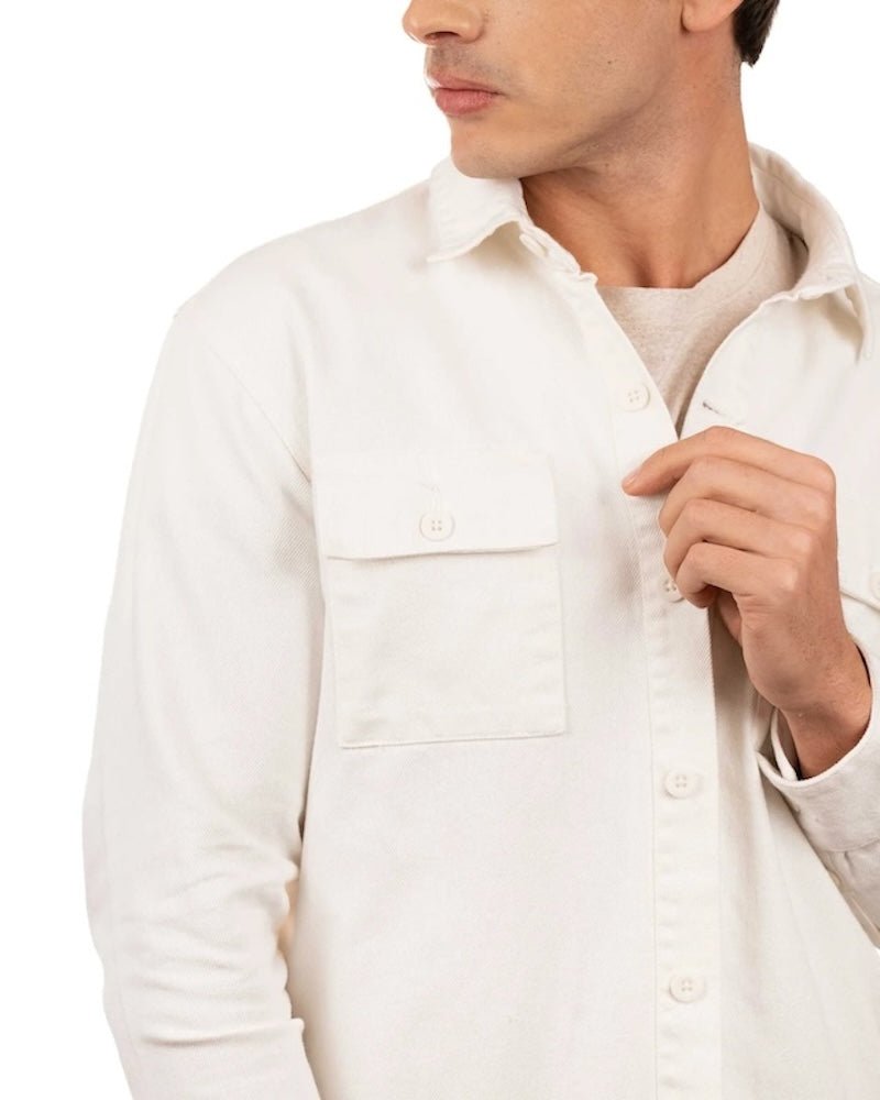 Close up of a man wearing a t-shirt and a white cotton jacket. He's standing behind a white background. The purpose of this image is to highlight the jacket, which is made in Colombia and available at EVAMAIA boutique.