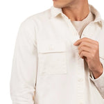 Close up of a man wearing a t-shirt and a white cotton jacket. He's standing behind a white background. The purpose of this image is to highlight the jacket, which is made in Colombia and available at EVAMAIA boutique.
