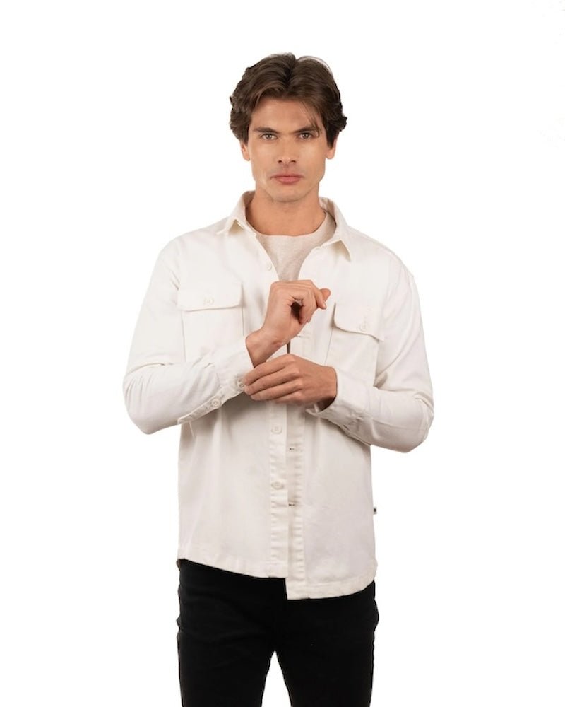Man wearing jeans, a t-shirt and a white cotton jacket. He's standing behind a white background. The purpose of this image is to highlight the jacket, which is made in Colombia and available at EVAMAIA boutique.