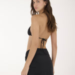 A woman modeling a black two-piece swimwear set consisting of a triangle bikini top and a high-waisted mini skirt with side ties, photographed against a plain white studio background.