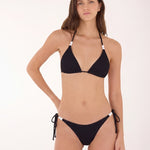 A woman modeling a black two-piece bikini with white accent beads at the halter straps and side-tie bottoms against a plain white studio background.