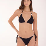 A woman modeling a black two-piece bikini with white accent beads at the halter straps and side-tie bottoms against a plain white studio background.