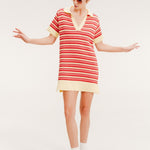 Woman wearing a short striped knit polo dress in red, coral, and pale yellow with a collared V-neck.