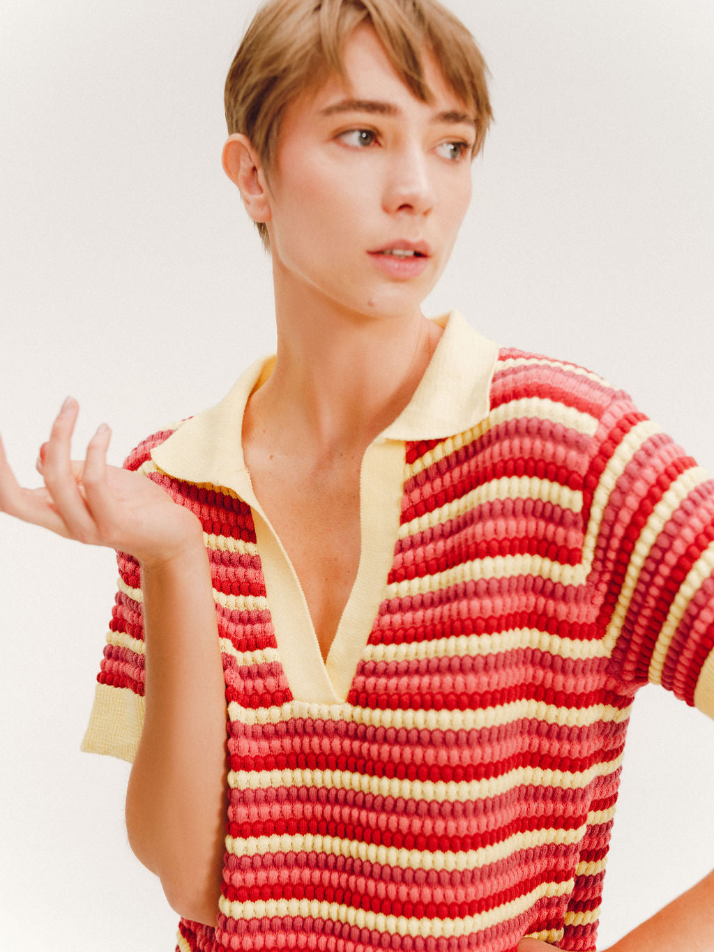 Close up of a woman wearing a short striped knit polo dress in red, coral, and pale yellow with a collared V-neck.