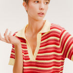 Close up of a woman wearing a short striped knit polo dress in red, coral, and pale yellow with a collared V-neck.