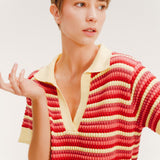 Close up of a woman wearing a short striped knit polo dress in red, coral, and pale yellow with a collared V-neck.