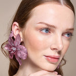 Woman wearing a purple floral earring against a neutral background