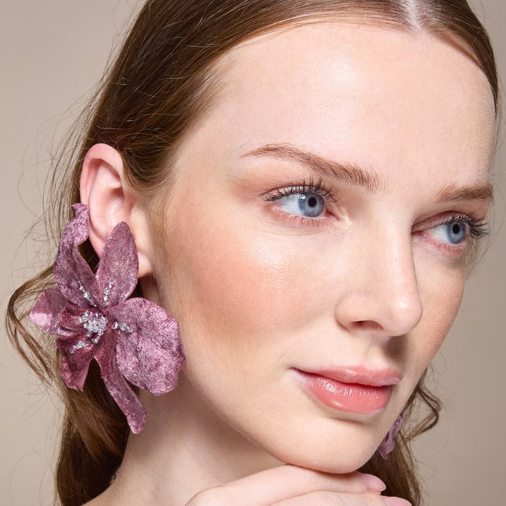 Woman wearing a purple floral earring against a neutral background