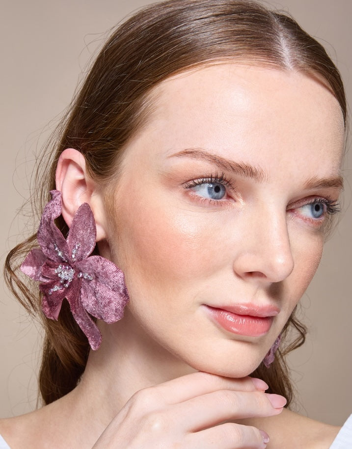 Woman wearing a purple floral earring against a neutral background
